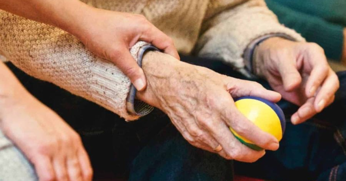 Close-up of an elderly person holding a small ball while another person gently supports their hand.