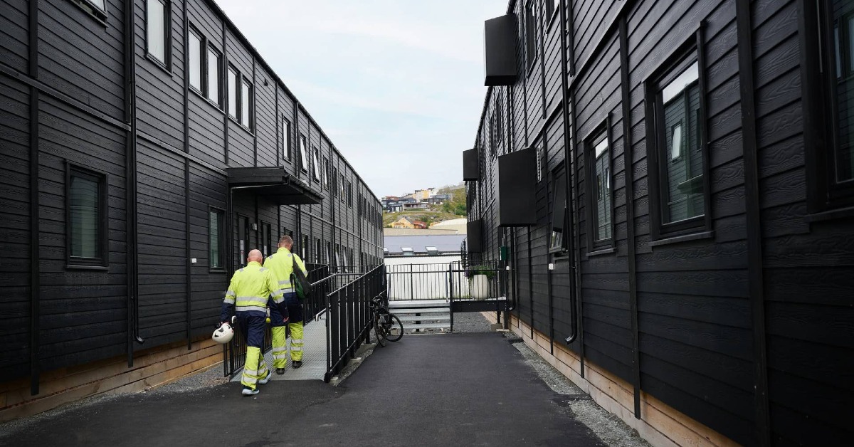 Workers walking between black modular accommodation buildings at a temporary camp site.