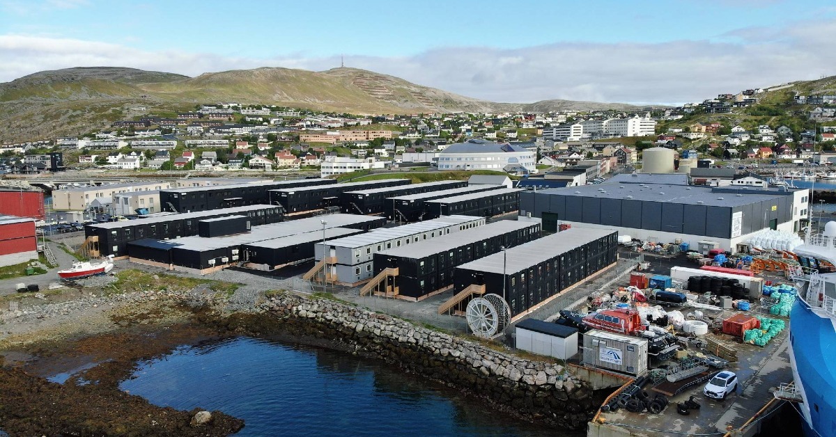 Aerial view of a temporary worker accommodation village by the waterfront in Hammerfest, with modular buildings, harbour facilities and surrounding hills in the background.