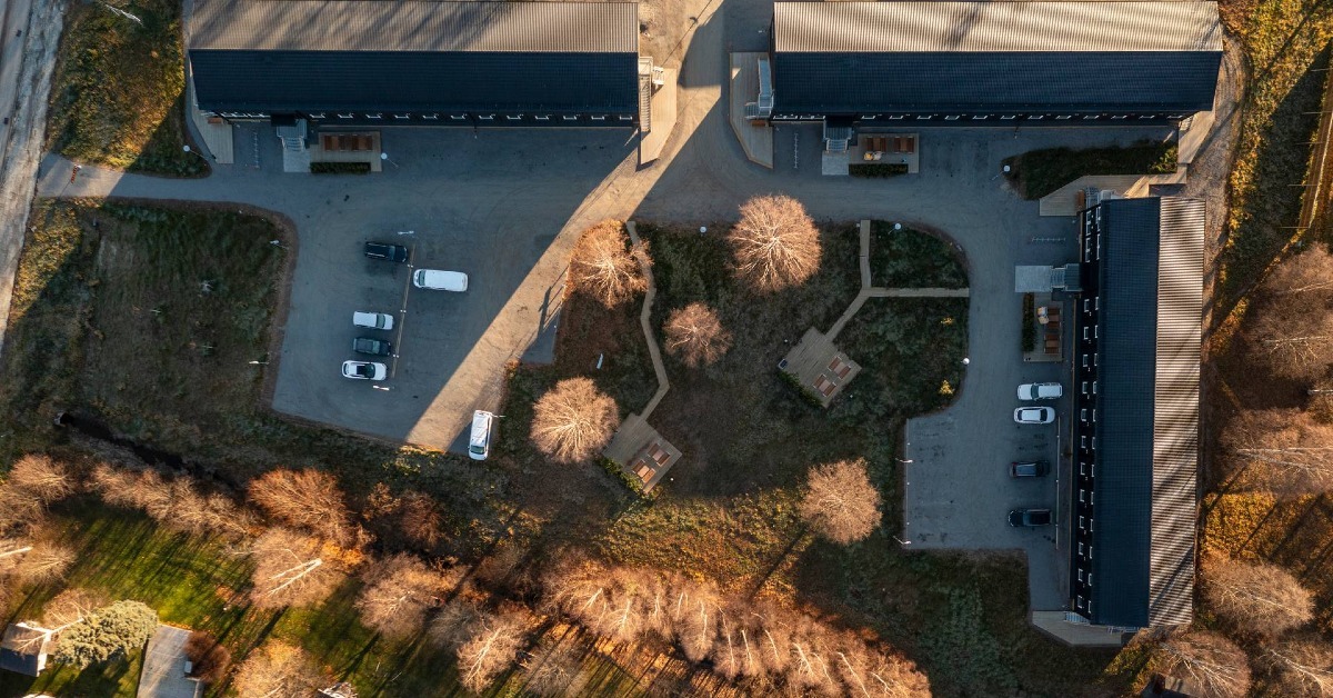 Aerial view of modular accommodation buildings arranged around paved roads, parking areas and landscaped outdoor seating spaces.